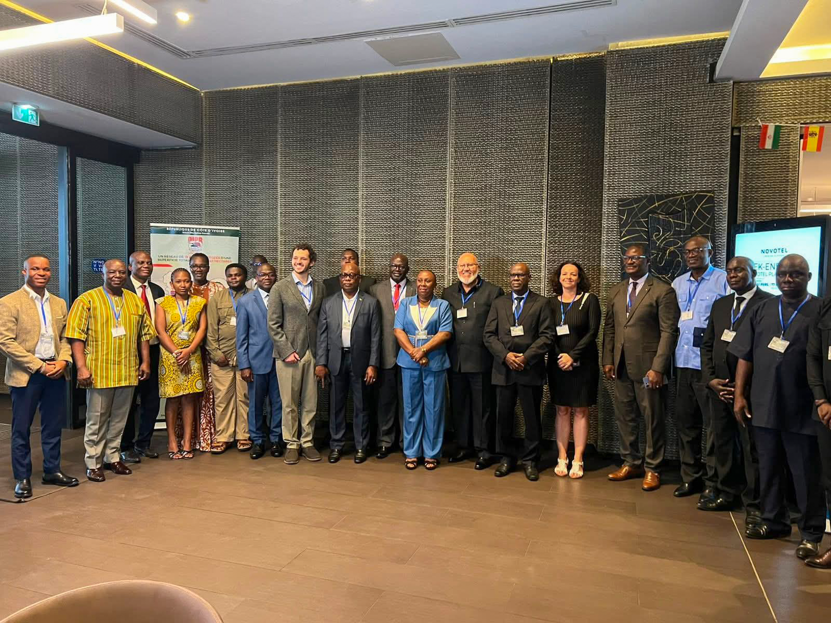 Group photograph of approximately 18 people standing together at an indoor conference venue.